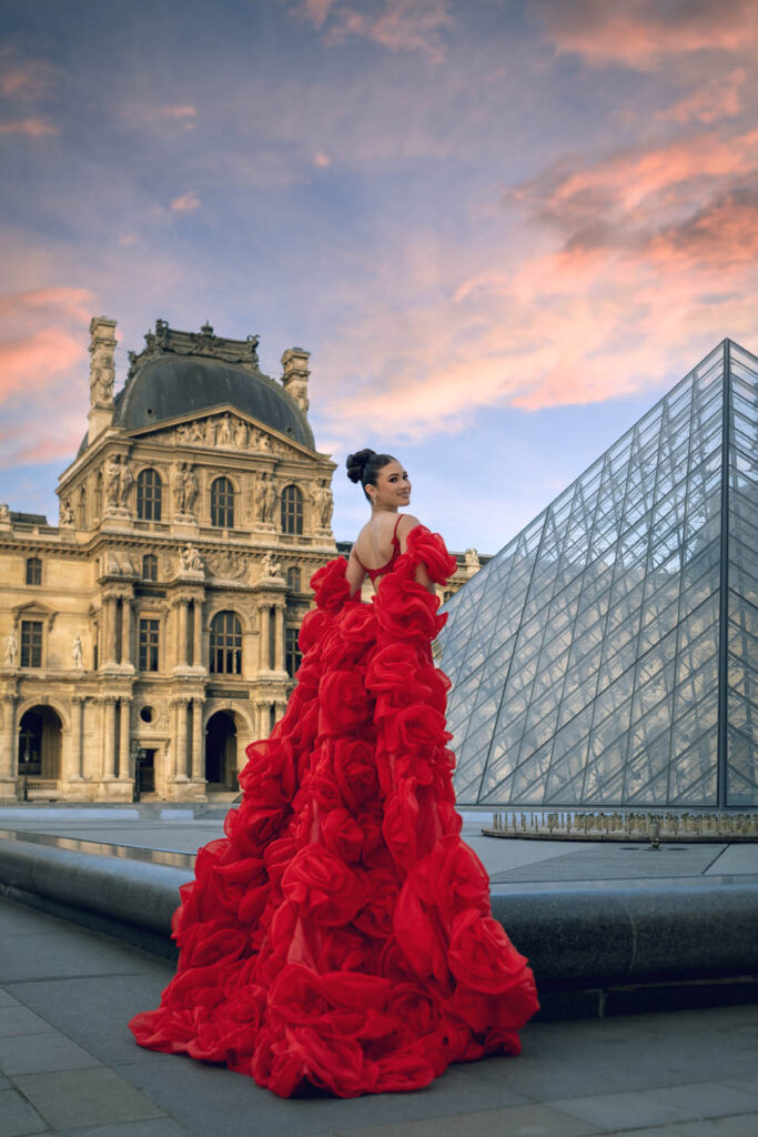 Quinceañera in a ruffled red gown posing by the Louvre Pyramid in Paris, France, by an Orlando destination photographer.