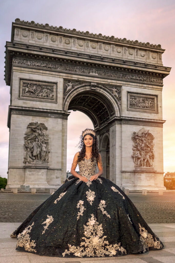 Quinceañera in a black and gold ballgown posing in front of the Arc de Triomphe in Paris, France, taken by an Orlando destination photographer.
