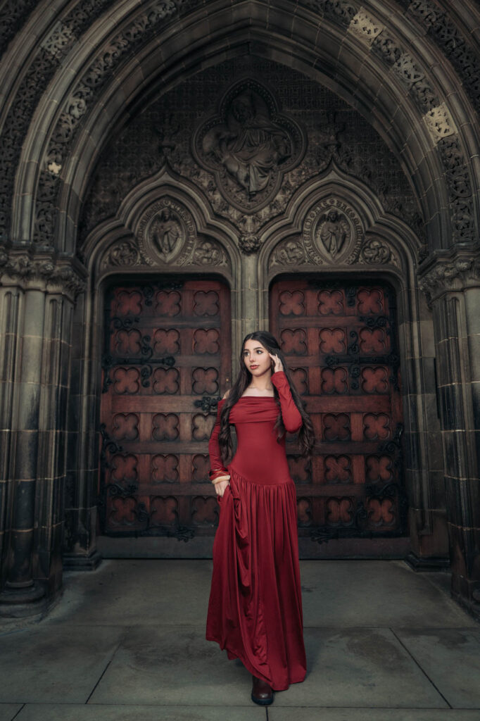 Quinceañera in a red gown before a gothic doorway in Edinburgh, Scotland