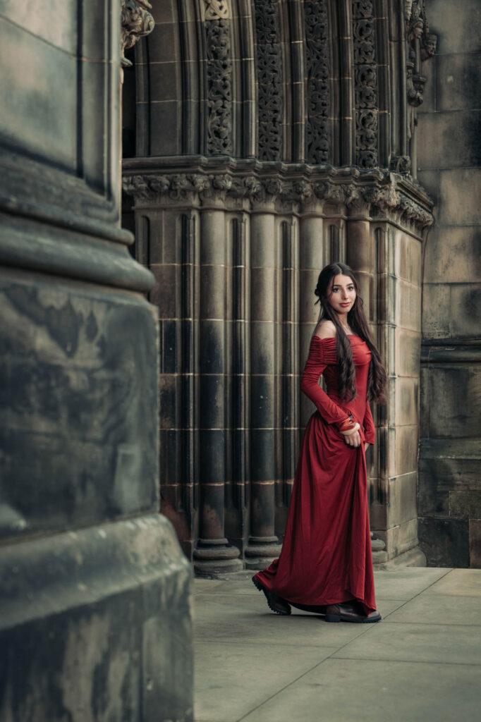 Quinceañera in a red gown beside carved gothic stonework in Edinburgh