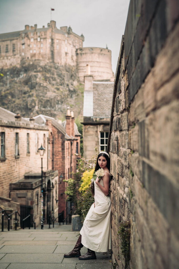 Quinceañera in a white dress with a yellow bouquet and Edinburgh Castle behind her
